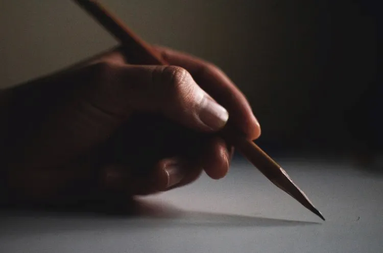 Hand holding a pencil, writing on paper